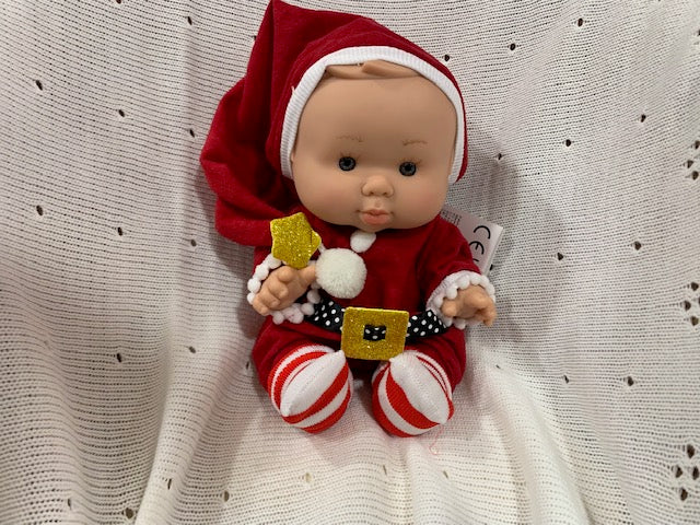 Baby doll in Christmas outfit with red hat, striped pants, and gold shoes on a textured white background.