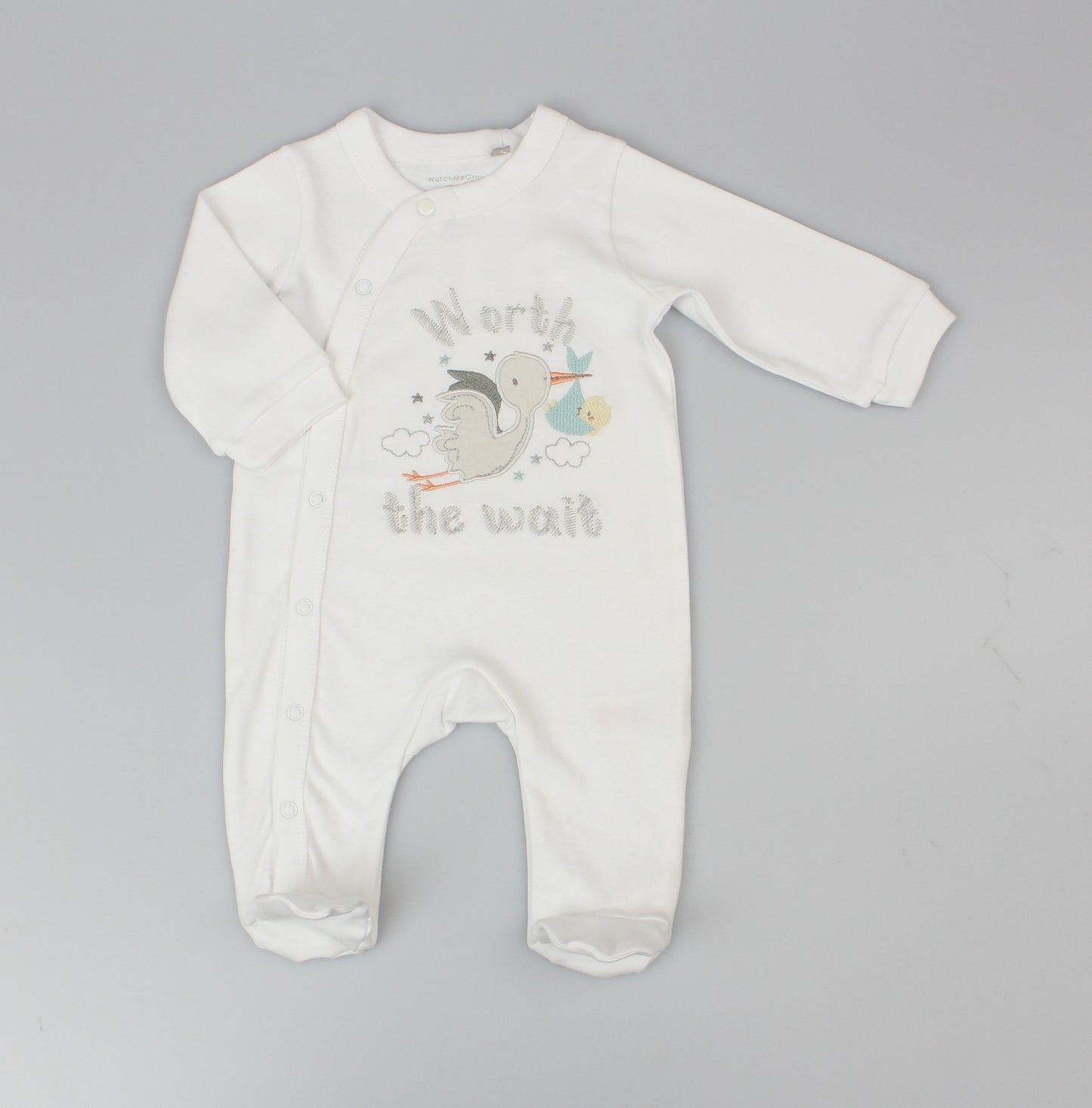 White Baby Sleepsuit With Worth The Wait Embroidery And An Applique Of A Stork Carrying A Baby